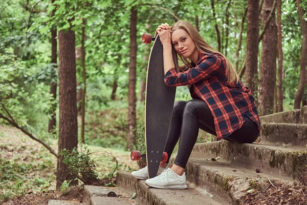 Giovane ragazza hipster bionda a riposo in un parco, dopo aver cavalcato sullo skateboard . — Foto Stock