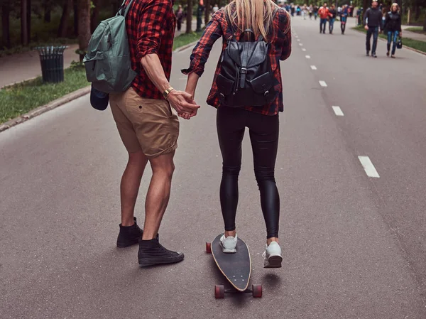 Jeune couple hipster. Guy apprend à sa copine à skater dans la rue dans un parc . — Photo