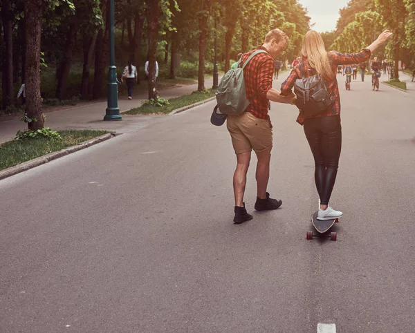 Unga hipster par. Killen lär hans flickvän att skateboard på gatan i en park. — Stockfoto