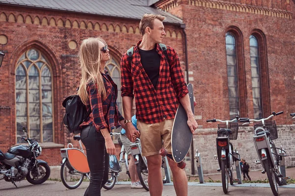 Молодая пара хипстеров, симпатичный фигурист и его девушка, гуляющие по старым улицам Европы . — стоковое фото