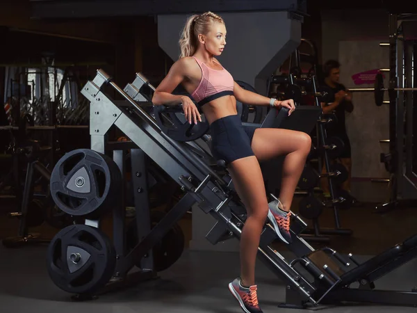 Sexig sportig kvinna i sportkläder liggande på en ben pressmaskin i gymmet. — Stockfoto