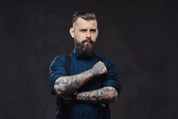 Retrato de un guapo hipster a la antigua con una camisa azul y tirantes, de pie con los brazos cruzados en un estudio . — Foto de Stock