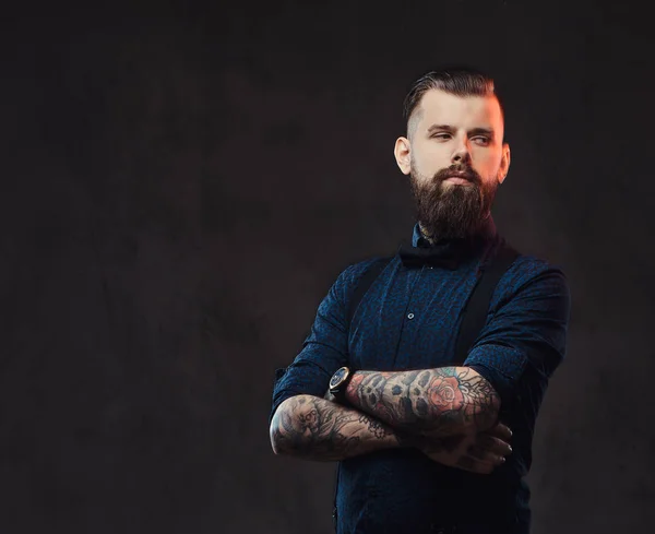 Retrato de um belo hipster à moda antiga com uma camisa azul e suspensórios, de pé com os braços cruzados em um estúdio . — Fotografia de Stock