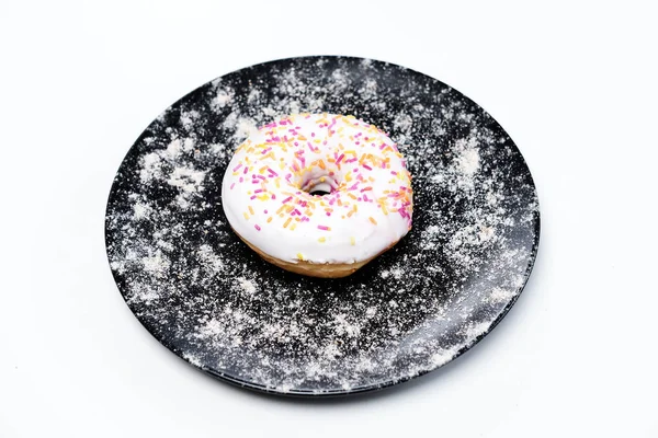 Appetizing donut with sprinkles lie on a black ceramic plate. — Stock Photo, Image