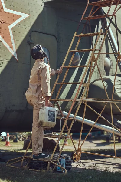 Mecânico em uniforme e capacete voador realiza manutenção de um grande helicóptero militar em um museu ao ar livre . — Fotografia de Stock