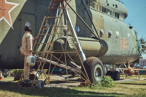 Mecánico en uniforme y casco volador lleva a cabo el mantenimiento de un gran helicóptero militar en un museo al aire libre . — Foto de Stock