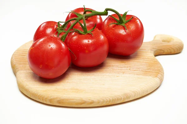 Varios tomates se encuentran en una tabla de cortar de madera . —  Fotos de Stock