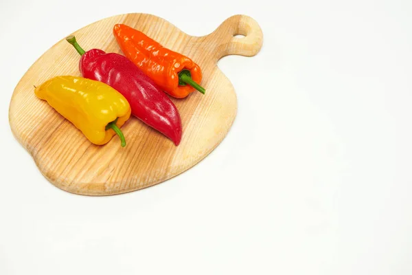 Verscheidene verschillende gekleurde paprika liggen op een houten snijplank. — Stockfoto