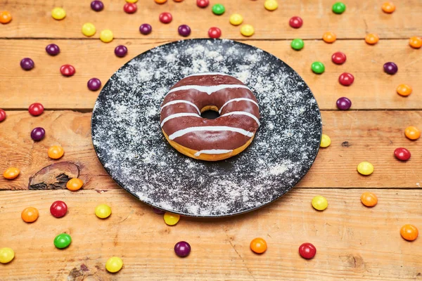 Appetizing chocolate donut lie on ceramic plate, sprinkled with colorful chocolate pellets. — Stock Photo, Image