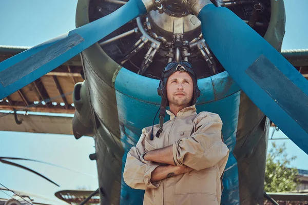 Valiente piloto guapo en un equipo de vuelo completo de pie con brazos cruzados cerca del avión militar . — Foto de Stock