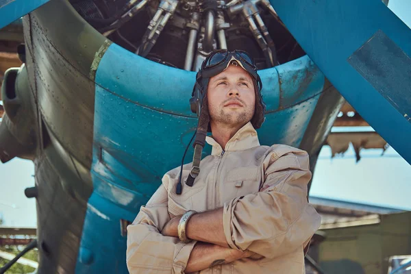 Valiente piloto guapo en un equipo de vuelo completo de pie con brazos cruzados cerca del avión militar . —  Fotos de Stock