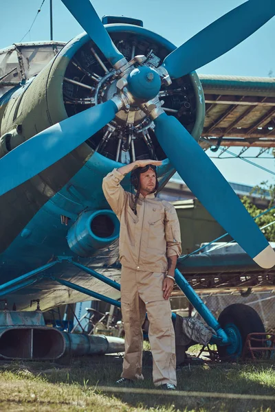 Доблестный красивый пилот в полном снаряжении стоит рядом с ретро-военным самолетом и отворачивается. . — стоковое фото