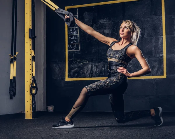 Sexy blonde Frau in Sportbekleidung beim Training mit Trx-System im Fitnessstudio. — Stockfoto