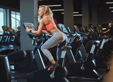 Sportif sarışın kadın modern fitness merkezinde bir egzersiz bisikleti üzerinde çalışma dışarı. Fitness yaşam spor kulübü.