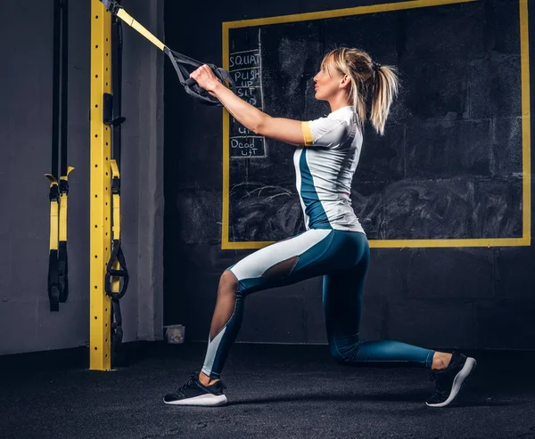 Sexy blondýnka v sportovní dělat cvičení s Trx systém v tělocvičně. — Stock fotografie