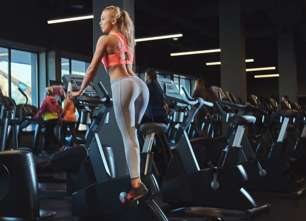 Sportive ξανθιά γυναίκα που εργάζονται έξω σε ένα ποδήλατο γυμναστικής στο σύγχρονο γυμναστήριο. Fitness lifestyle στην αθλητική λέσχη. — Φωτογραφία Αρχείου