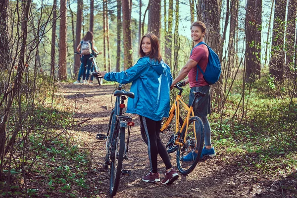 Group of young friends hiking through the forest with bikes on a beautiful summer day