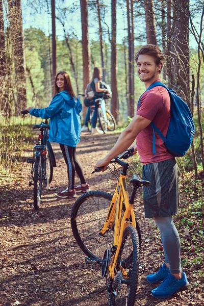 Group of young friends hiking through the forest with bikes on a beautiful summer day