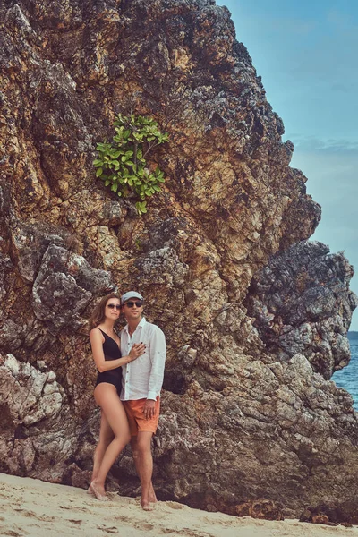 Casal atraente posando em uma praia perto de grandes pedras de recife, goza de umas férias em uma bela ilha . — Fotografia de Stock