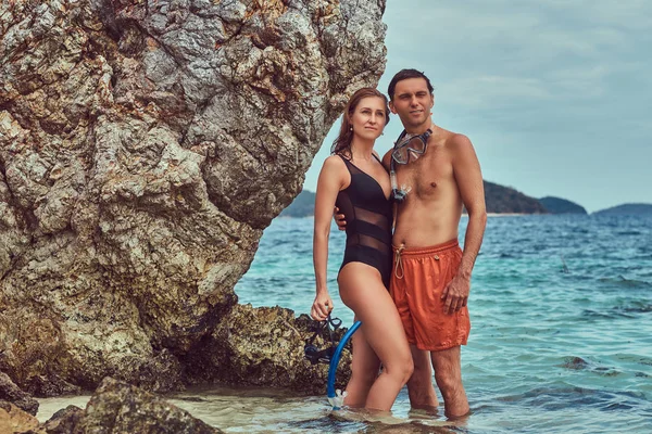 Casal atraente posando em uma praia perto de grandes pedras de recife, goza de umas férias em uma bela ilha . — Fotografia de Stock