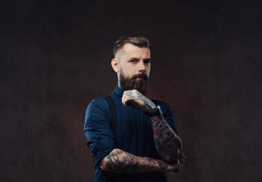 Mavi bir gömlek ve pantolon askısı, çene bir stüdyoda el ile ayakta dalgın yakışıklı eski moda hippi. Karanlık bir arka plan üzerinde izole.