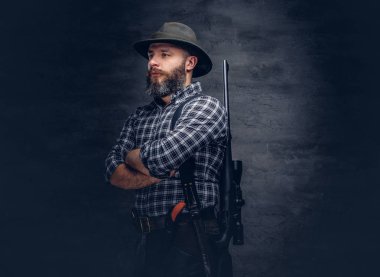 Sakallı bir avcı bir polar gömlek ve şapka ayakta arkasından bir tüfekle portresi. Karanlık bir arka plan üzerinde izole. 