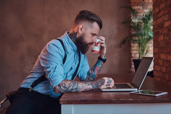 Handsome Tattooed Hipster Shirt Suspenders Sitting Desk Working Laptop Holds — Stock Photo, Image