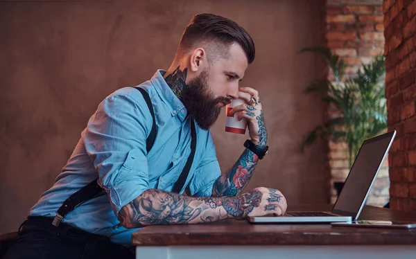 Handsome Tattooed Hipster Shirt Suspenders Sitting Desk Working Laptop Holds — Stock Photo, Image