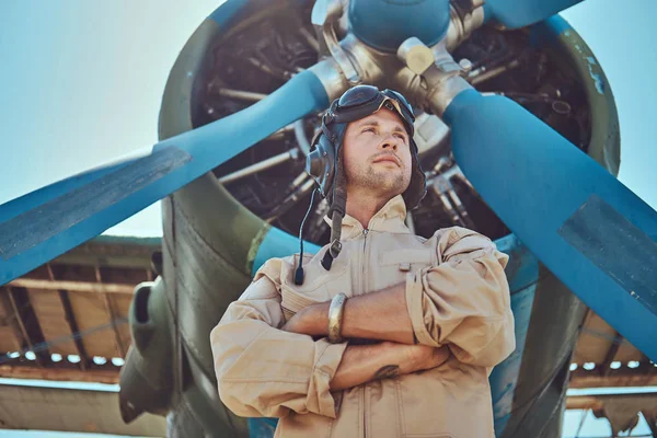 英俊的飞行员在一个完整的飞行装备站立与横渡的胳膊在军用飞机附近 — 图库照片
