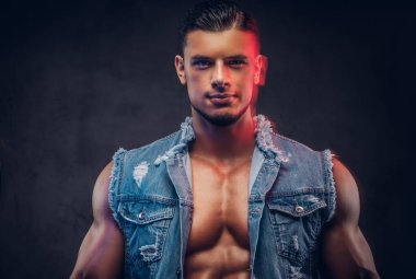 Seksi çıplak moda kendine güvenen erkek denim yelek kaslı bir vücut ile bir stüdyoda teşkil etmektedir. Koyu arka plan üzerinde izole.