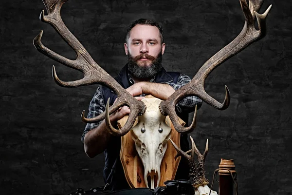 Bearded hunter in a fleece shirt and hat with his trophies. Isolated on a dark background.
