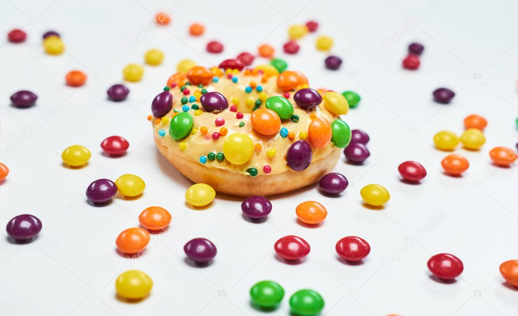 Appetizing golden donut sprinkled with colorful chocolate pellets. Isolated on white background.