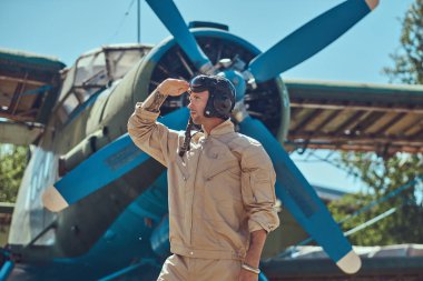 Tam bir uçuş yiğit yakışıklı pilot ayakta retro askeri uçak yakınındaki Dişli ve uzak görünüyor.