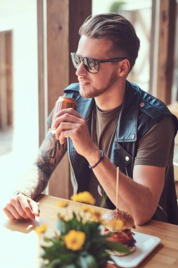 Bir şık saç ve sakal ile yakışıklı hipster yol kenarına yerleştirilen bir kafede öğle yemeği için durdu bir masada oturur.