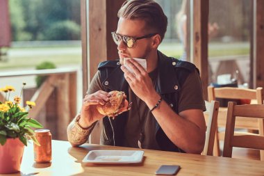 Bir hamburger yeme hipster şık saç ve sakal ile yol kenarına yerleştirilen bir kafede yemek yemeye karar verdim bir masada oturur.