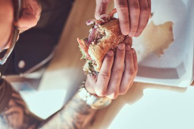 Bir şık saç ve sakal aç hipster adamla yakın çekim portre bir hamburger yeme yol kenarına yerleştirilen bir kafede yemek yemeye karar verdim bir masada oturur.