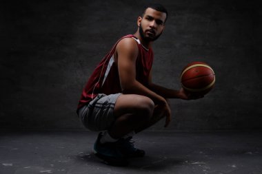 Bir top ile çömelme spor giyim, Afrikalı-Amerikalı basketbol oyuncusu. Koyu arka plan üzerinde izole. 