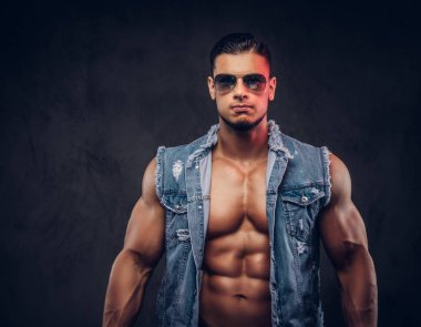 Seksi çıplak moda spor adam kot yelek ve güneş gözlüğü bir stüdyoda teşkil etmektedir..