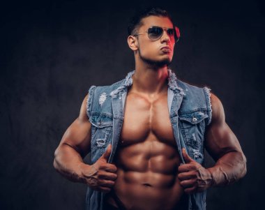 Seksi çıplak moda spor adam kot yelek ve güneş gözlüğü bir stüdyoda teşkil etmektedir..