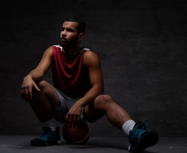 Spor giyim bir top karanlık bir arka plan üzerinde oturan genç Afro-Amerikan basketbol oyuncusu.