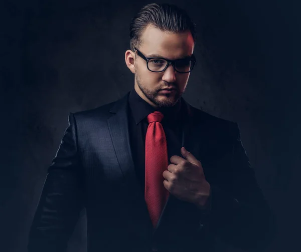 一个神秘的时尚男性在黑色西装和红色领带的肖像。在黑暗背景下被隔离. — 图库照片