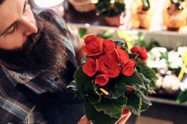 Sakal ve dövme elinde üniforması ile profesyonel erkek çiçekçi bir buket çiçek ile pota çiçekçide tutar..