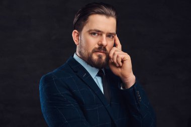 Dalgın orta yaşlı adam sakal ve saç modeli ile zarif mavi takım elbise giymiş. Bir stüdyoda dokulu koyu arka plan üzerinde izole. 