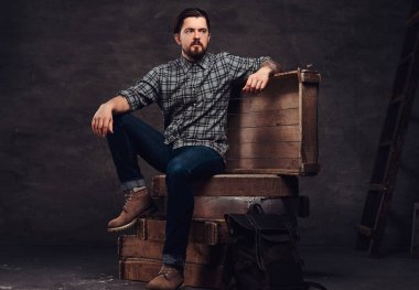 Kareli gömlek ve kot, ahşap kutular bir stüdyoda oturup tattoed orta yaş hipster adam portresi tam vücut giymiş.