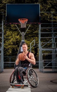 Tekerlekli sandalyede kötürüm basketbol oyuncusu bir topu bir açık oyun yere tutuyor..