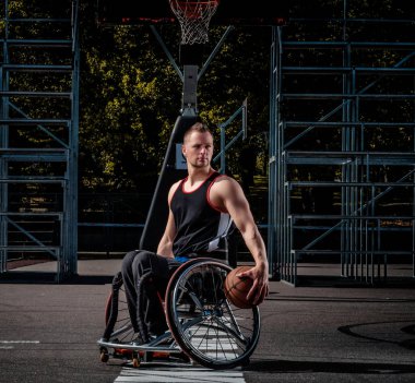 Tekerlekli sandalyede kötürüm basketbol oyuncusu bir topu bir açık oyun yere tutuyor..