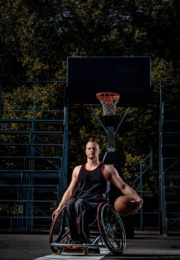 Tekerlekli sandalyede kötürüm basketbol oyuncusu bir topu bir açık oyun yere tutuyor..