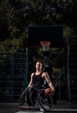 Tekerlekli sandalyede kötürüm basketbol oyuncusu bir topu bir açık oyun yere tutuyor..