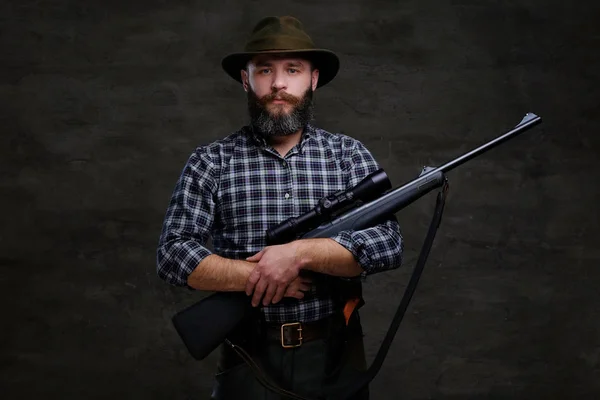 Guapo cazador barbudo viajero en una camisa de lana y sombrero sostiene rifle con una vista . —  Fotos de Stock