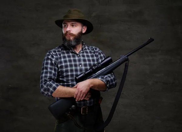 Bonito caçador barbudo viajante em uma camisa de lã e chapéu segura rifle com uma visão . — Fotografia de Stock